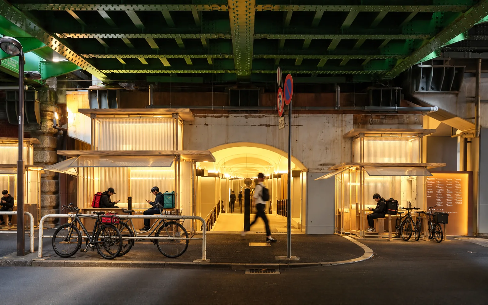 A connected row of illuminated rider facilities beneath an elevated railway.